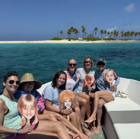 A lively group of friends enjoys a fun boat trip, holding playful cutouts while surrounded by stunning island scenery — perfect for memorable adventures on the water.