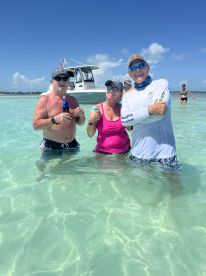 A cheerful group enjoys drinks while standing in shallow water, with a boat anchored nearby — perfect for a fun sandbar stop experience.
