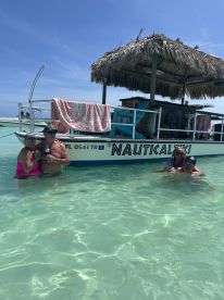 A joyful group enjoys a refreshing swim around a pontoon boat named 'Nautical Tiki' in crystal-clear waters, perfect for a fun day out on the water.