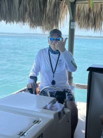 A captain gives a thumbs up from the helm of a boat, showcasing the interior console and a beautiful turquoise backdrop — perfect for a day on the water.