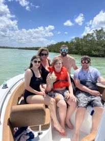 A cheerful family poses on a boat, showcasing a fun day out on the water with a beautiful backdrop of nature.
