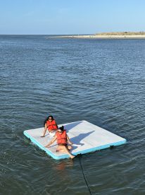 Two friends enjoy a sunny day on a floating mat in the water, showcasing a perfect summer getaway filled with fun and relaxation.