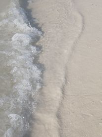 A close-up view of waves lapping against the sandy shore, capturing the serene essence of a beach setting.
