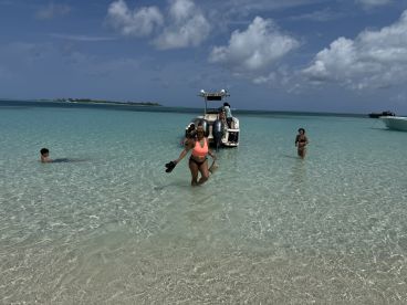 A lively group enjoys a day at the beach, swimming and relaxing in the clear waters, with a pontoon boat anchored nearby — perfect for a fun-filled day on the water.