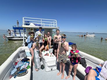 A joyful group of friends and family enjoy refreshing cocktails on a pontoon boat, celebrating under the sun while swimming in the clear waters — perfect for summer fun and memorable gatherings.