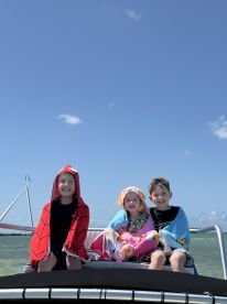 Three children enjoy a sunny day on a boat, wrapped in colorful towels, capturing the joy of a fun-filled day on the water.