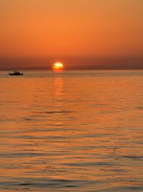 A stunning sunset over the water with a silhouette of a boat in the foreground, capturing the serene beauty of evening cruises.