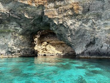 A stunning view of a rocky coastline with a cave entrance, surrounded by crystal-clear turquoise waters — a picturesque destination for boat tours and exploration.