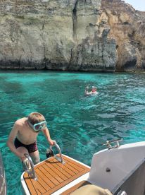 A young boy climbs aboard while another person enjoys a swim in the crystal-clear waters, showcasing a fun family day on the boat.