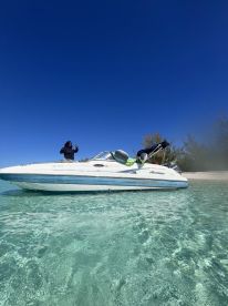 A person gestures from a boat in crystal-clear waters, showcasing a perfect day on the water near a beautiful beach.
