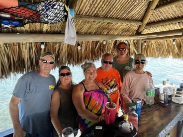A cheerful group gathers at a tiki bar, enjoying drinks and good company — perfect for a fun day on the water.