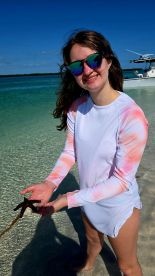 A young girl joyfully holds a starfish in shallow waters, showcasing a delightful moment of human-animal interaction in a tropical setting.