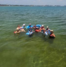 A lively group enjoys a fun day in the water, floating with drinks and soaking up the sun — the perfect recipe for a memorable beach outing.