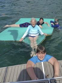 A joyful group enjoys a sunny day on a floating mat in the water, showcasing family fun and relaxation during their boating adventure.
