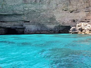 A stunning view of a rocky coastline with a cave entrance, surrounded by vibrant turquoise waters — perfect for exploring hidden gems on a boating adventure.