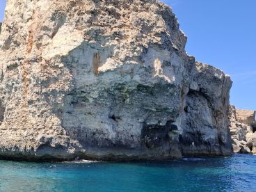 A rocky cliffside is captured against a backdrop of clear blue waters, but the image lacks clarity and detail.
