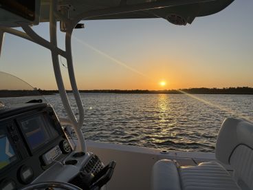 A serene view from the helm of a boat at sunset, showcasing the tranquil waters and the warm glow of the setting sun — perfect for evening cruises.