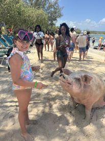 A young girl feeds a friendly pig on the beach, showcasing a delightful interaction with wildlife — a memorable experience in the Bahamas.