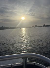A serene sunset view over the water, captured from the deck of a boat, showcasing the tranquil beauty of the evening sky and reflections on the surface.