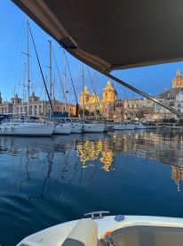 A serene evening view of a marina, showcasing boats and the beautiful reflections of illuminated buildings in the water — a picturesque scene perfect for evening boat tours.
