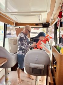 A child is assisted by an adult in putting on a life jacket inside the cabin of a boat, emphasizing safety and preparation for a fun day on the water.