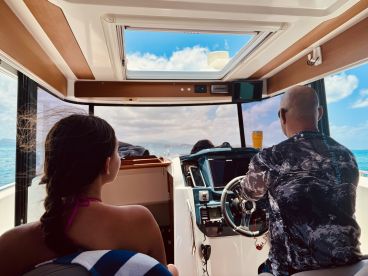 A view from inside the cabin of a boat, featuring a child and an adult at the helm, enjoying a day on the water. The modern interior showcases the boat's helm and seating area.