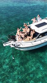 A lively group of friends enjoys a fun day on the water, waving from their boat in crystal-clear waters — perfect for summer celebrations and adventures.