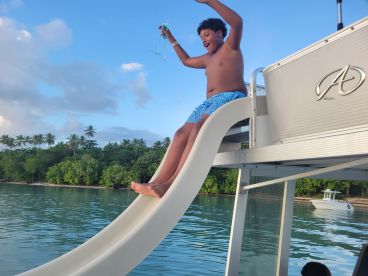 A young boy joyfully slides off a boat into the water, capturing the excitement of summer fun and water activities. Perfect for family outings and adventure on the water.