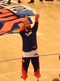 An unclear image of a person on a basketball court, possibly during warm-ups. The focus is not sharp, making it difficult to identify the scene.