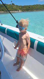 A young child stands on the deck of a boat, ready for snorkeling in the clear turquoise waters — a perfect moment for family adventures on the water.