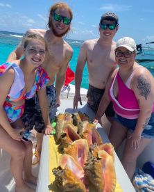 A group of friends proudly displays their catch of conch shells while enjoying a sunny day on the water — a perfect highlight of their snorkeling adventure.