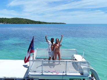 A joyful couple poses on the deck of a boat, celebrating under the sun with stunning ocean views in the background — perfect for memorable summer adventures.