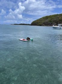 A woman enjoys a relaxing swim on a paddleboard in crystal-clear waters, surrounded by scenic views — a perfect moment for beach fun and relaxation.