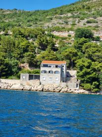 A view of a coastal building surrounded by lush greenery, set against a backdrop of clear blue waters. The image captures a serene landscape, ideal for exploring coastal architecture.