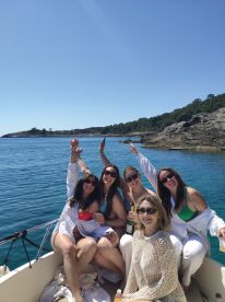 A joyful group of friends celebrates on a boat, raising their glasses of champagne against a stunning coastal backdrop — perfect for memorable summer outings.