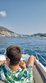 A young man enjoys a refreshing drink while relaxing on the boat, with a scenic view of the coastline in the background — perfect for a leisurely day on the water.
