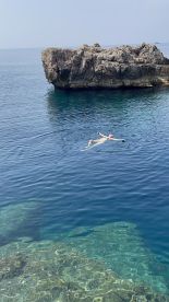 A person floats serenely in the crystal-clear waters near a rocky outcrop, showcasing the beauty of a tranquil swimming experience in nature.