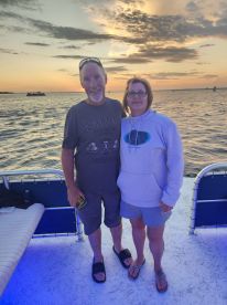 A cheerful couple poses for a photo on a boat during sunset, capturing a memorable moment on the water — perfect for romantic getaways or special celebrations.