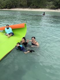 A joyful family enjoys a day in the water, playing on a floating mat and creating lasting memories in a tropical paradise.