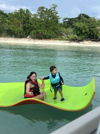 A joyful moment as a mother and her child enjoy a fun water activity on a floating mat, showcasing family bonding in a beautiful aquatic setting.