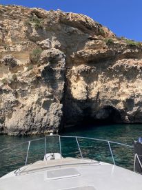 A stunning view from the front of a boat navigating along a rocky coastline, showcasing the natural beauty of the cliffs and clear waters.