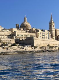 A stunning view of the historic architecture along the coastline, showcasing the iconic dome and spires against a clear blue sky — a perfect backdrop for exploring Malta's rich heritage.