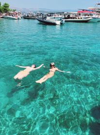 A couple enjoys a refreshing swim in crystal-clear waters, surrounded by boats — a perfect summer escape in a picturesque setting.