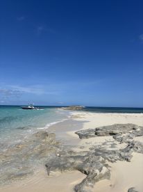 A picturesque view of a secluded beach with a boat cruising along the coastline, showcasing the stunning turquoise waters and rocky shoreline — perfect for a day of relaxation and exploration.