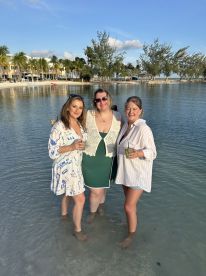 Three friends enjoy cocktails while wading in shallow water, capturing a joyful beach celebration perfect for memorable moments with loved ones.