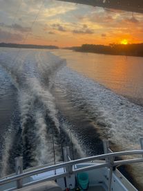 A stunning sunset view from the helm of a boat, showcasing the tranquil waterway and fishing rods in the foreground — perfect for evening cruises and fishing adventures.