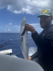 A fisherman proudly displays his catch aboard a boat in the open ocean, showcasing the thrill of deep-sea fishing adventures.