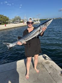 A woman proudly displays her catch of a barracuda after a successful fishing trip, showcasing the thrill of deep-sea fishing adventures.