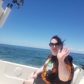 A cheerful individual waves from the deck of a boat, enjoying a sunny day on the ocean — perfect for memorable boating adventures.
