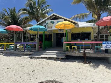 A colorful beachside establishment with umbrellas and seating, perfect for enjoying a tropical atmosphere. The scene captures a relaxed vibe, ideal for visitors looking to unwind by the shore.